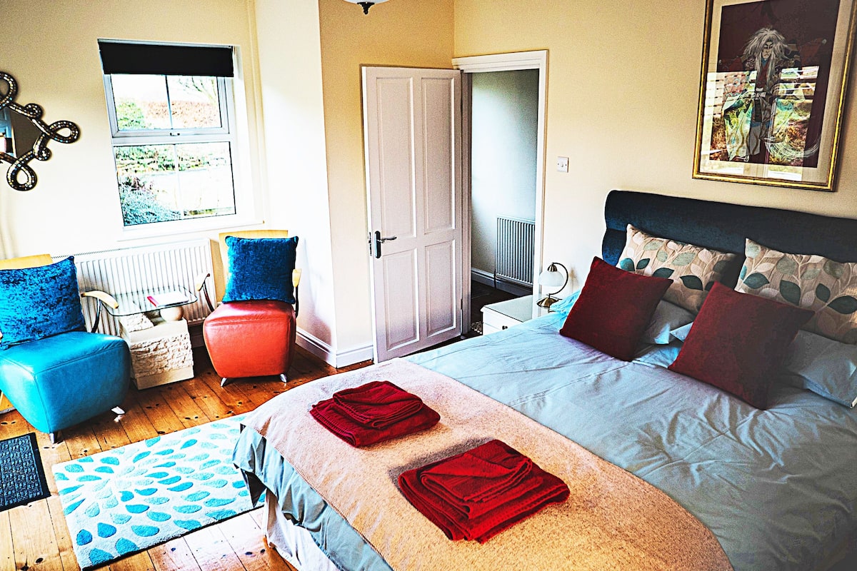 Um quarto com uma cama, uma cadeira, um sofá e uma porta que dá para outro cômodo.