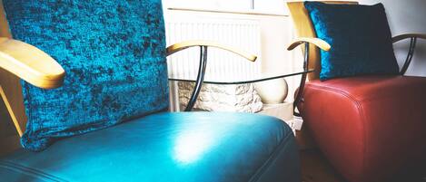 Two chairs with wooden armrests and blue cushions, placed near a window with a view of a stone wall and a radiator.