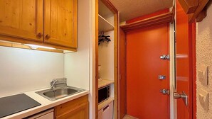A compact kitchen with wooden cabinets, a stainless steel sink, and a red door leading to a storage area.