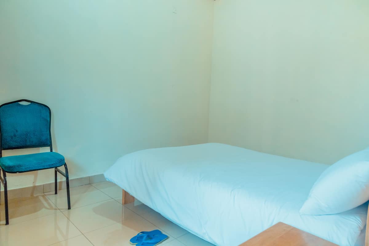 Een kamer met een bed, een stoel en een paar slippers op de vloer.