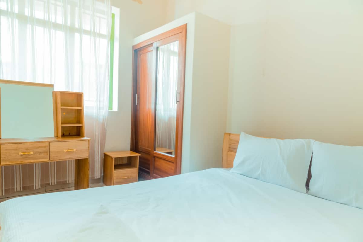 Een slaapkamer met een bed, een houten dressoir en een kledingkast.