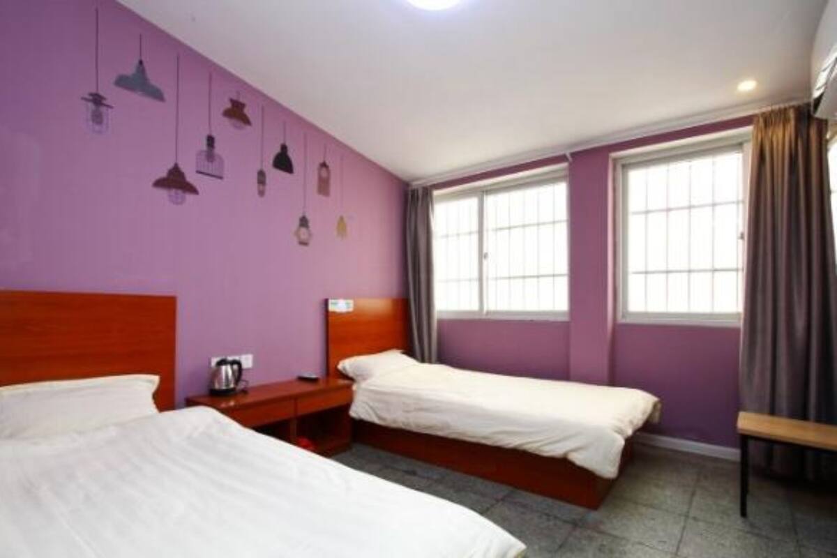 Ein Zimmer mit zwei Einzelbetten, einem Holz-Kopfteil, einem kleinen Nachttisch mit Lampe und einem Fenster mit Vorhängen.