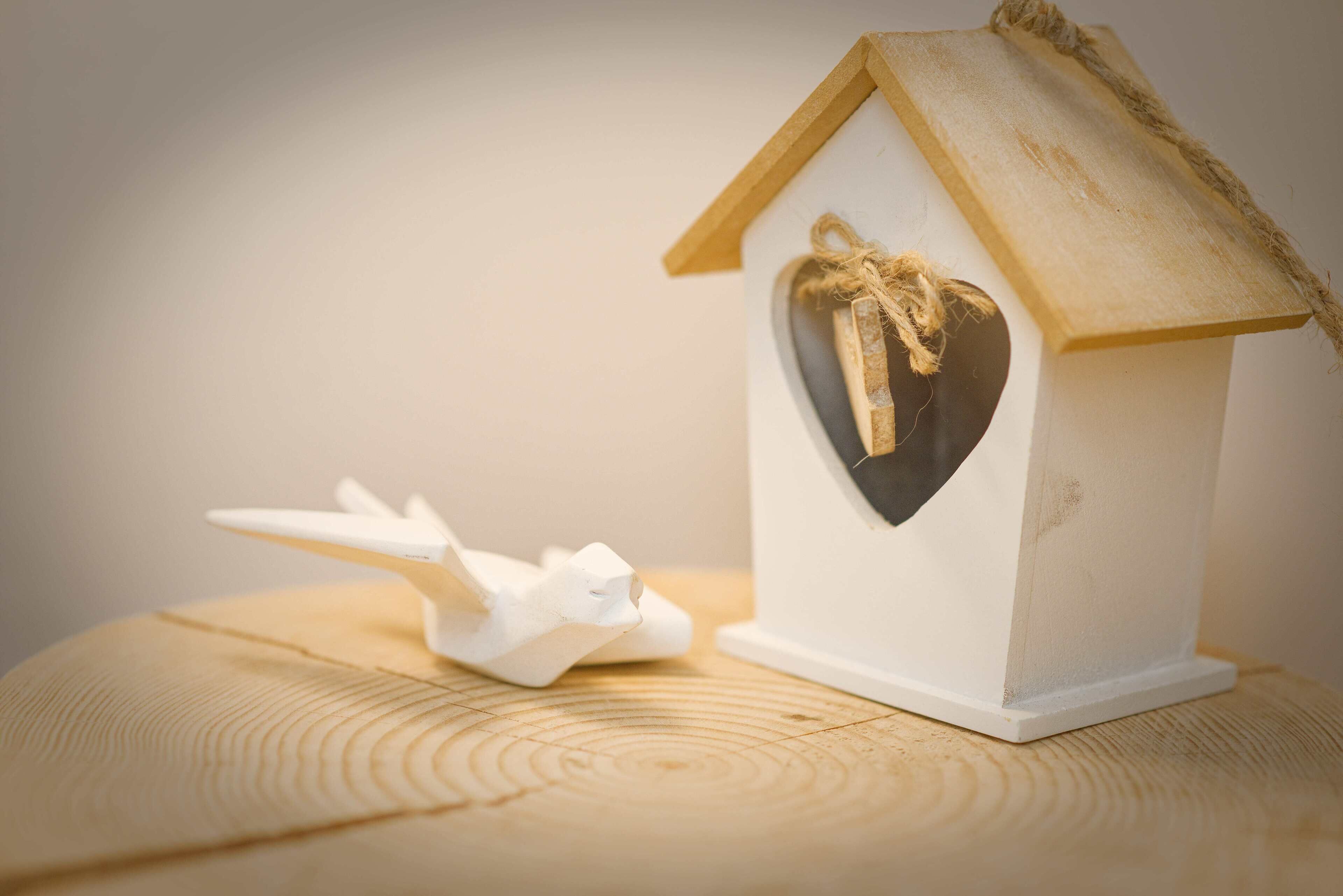 A small white birdhouse with a heart-shaped window and a rope tied around the roof.