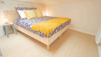 Un dormitorio con una cama de madera, ropa de cama floral, un plaid amarillo, una mesita de noche con una lámpara y una pared con textura.