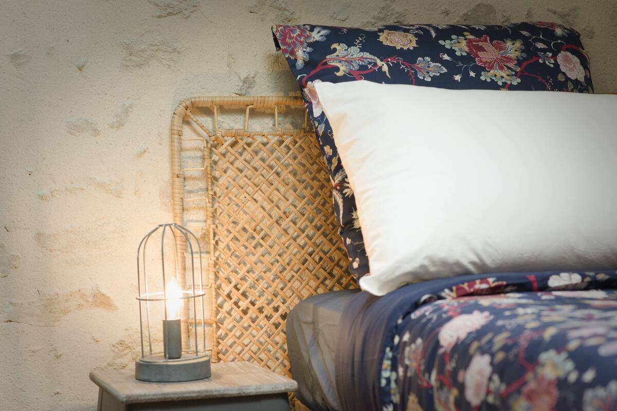 Una cama con colcha estampada con motivos florales, un almohajar blanco y un cabecero de mimbre.