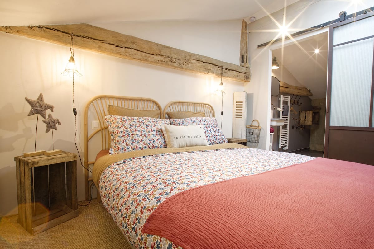 Un dormitorio con techo de madera, una cama con ropa de cama floral y una manta roja.