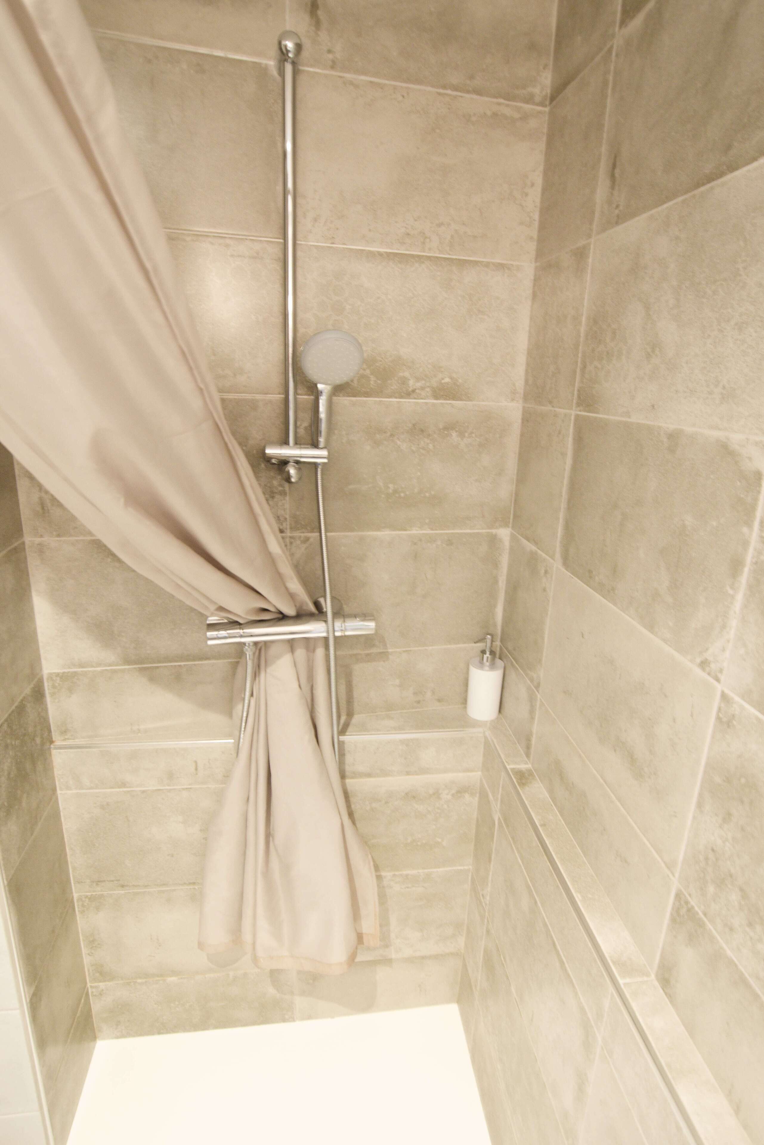 Eine Dusche mit beigen Fliesen, einem Duschvorhang und einer Handbrause.