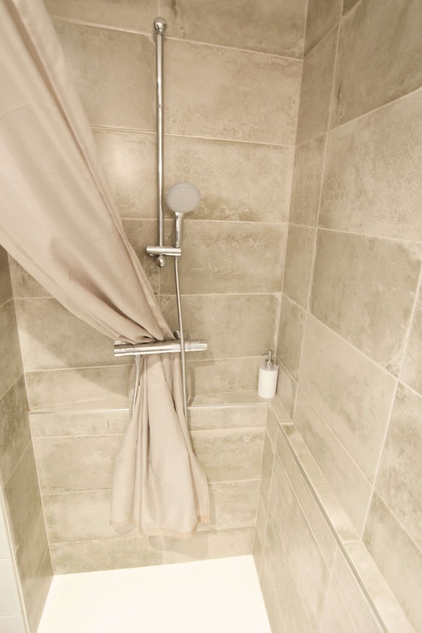 A shower with beige tiles, a shower curtain, and a handheld showerhead. - La Belle lurette (Bressuire)