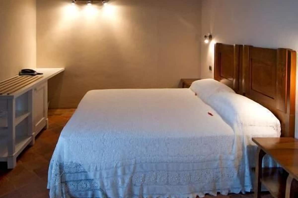 Un dormitorio con techo de madera, una cama con ropa de cama blanca, una mesita de noche y una mesita auxiliar.