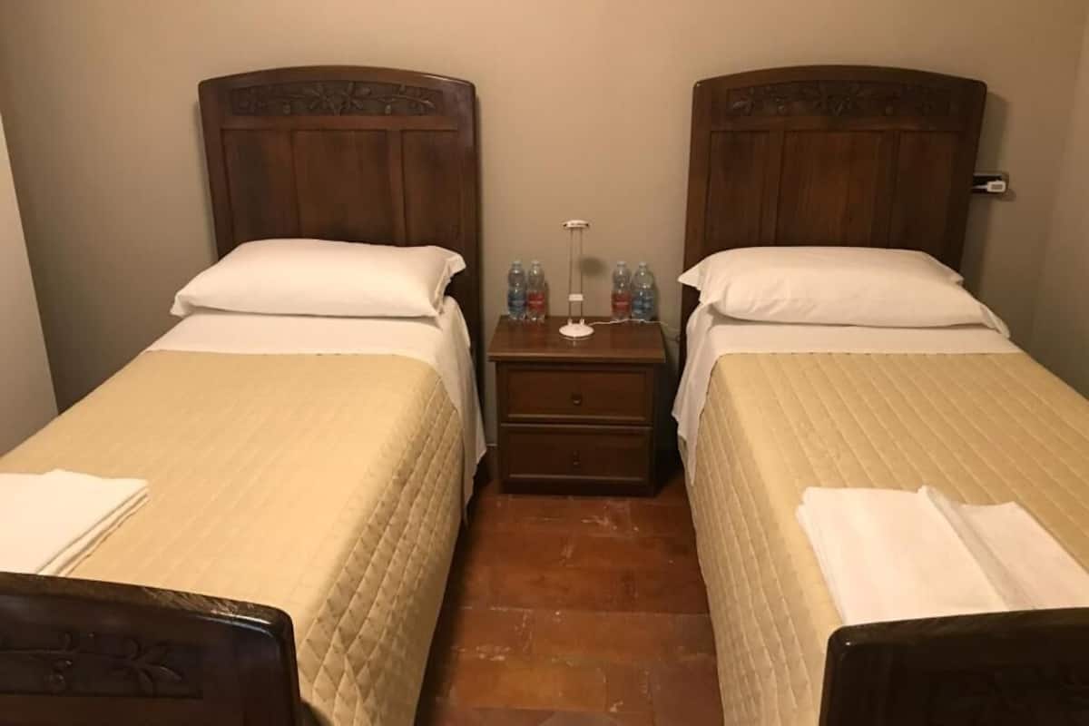 Habitación doble con dos camas, una mesita de noche con lámpara y un cajón pequeño.