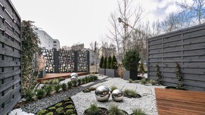 A modern outdoor garden with a wooden deck, decorative metal spheres, and a variety of plants. - City of The Kings Arianska Garden (Kraków)