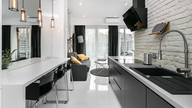 A modern kitchen with a white countertop, black cabinets, and a built-in oven. There is a dining area with a white table and black chairs. - City of The Kings Arianska Garden (Kraków)