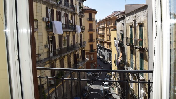 A narrow street with buildings on either side, balconies with laundry hanging, and parked cars. - La Baia di Napoli (Naples)