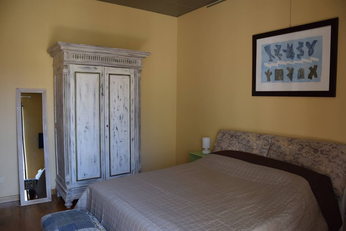 A bedroom with a large bed, a wardrobe, a framed artwork on the wall, and a mirror.