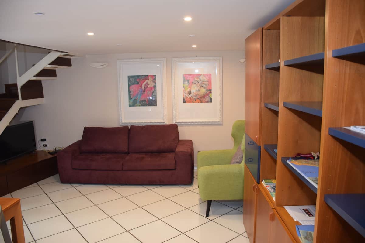 A living room with a brown sofa, a green armchair, and a wooden bookshelf.