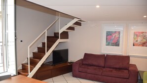 A modern living room with a wooden staircase, a flat-screen TV, a red sofa, and two framed artworks on the wall. - La Baia di Napoli (Naples)