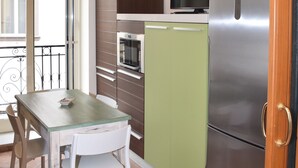 A compact kitchen with a refrigerator, microwave, and oven. There is a dining table with chairs and a window with a view. - La Baia di Napoli (Naples)