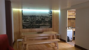 Una sala de estar con un banco de madera, un sofá rojo y una mesa de comedor. En la pared, un cuadro con una vista urbana.
