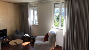 Una habitación con techo de madera, un sofá, una mesa redonda, un televisor y una ventana con cortinas.