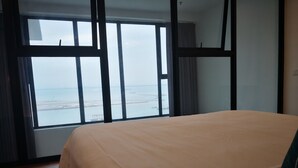 A bedroom with a large window, wooden floor, and a bed with a beige bedspread. - Casa Duplex at Sunrise Gurney Seaview (George Town)