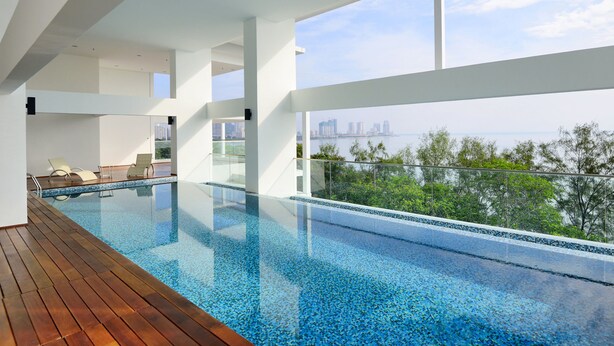 A modern indoor swimming pool with a wooden deck, glass railings, and a city view. - Casa Duplex at Sunrise Gurney Seaview (George Town)
