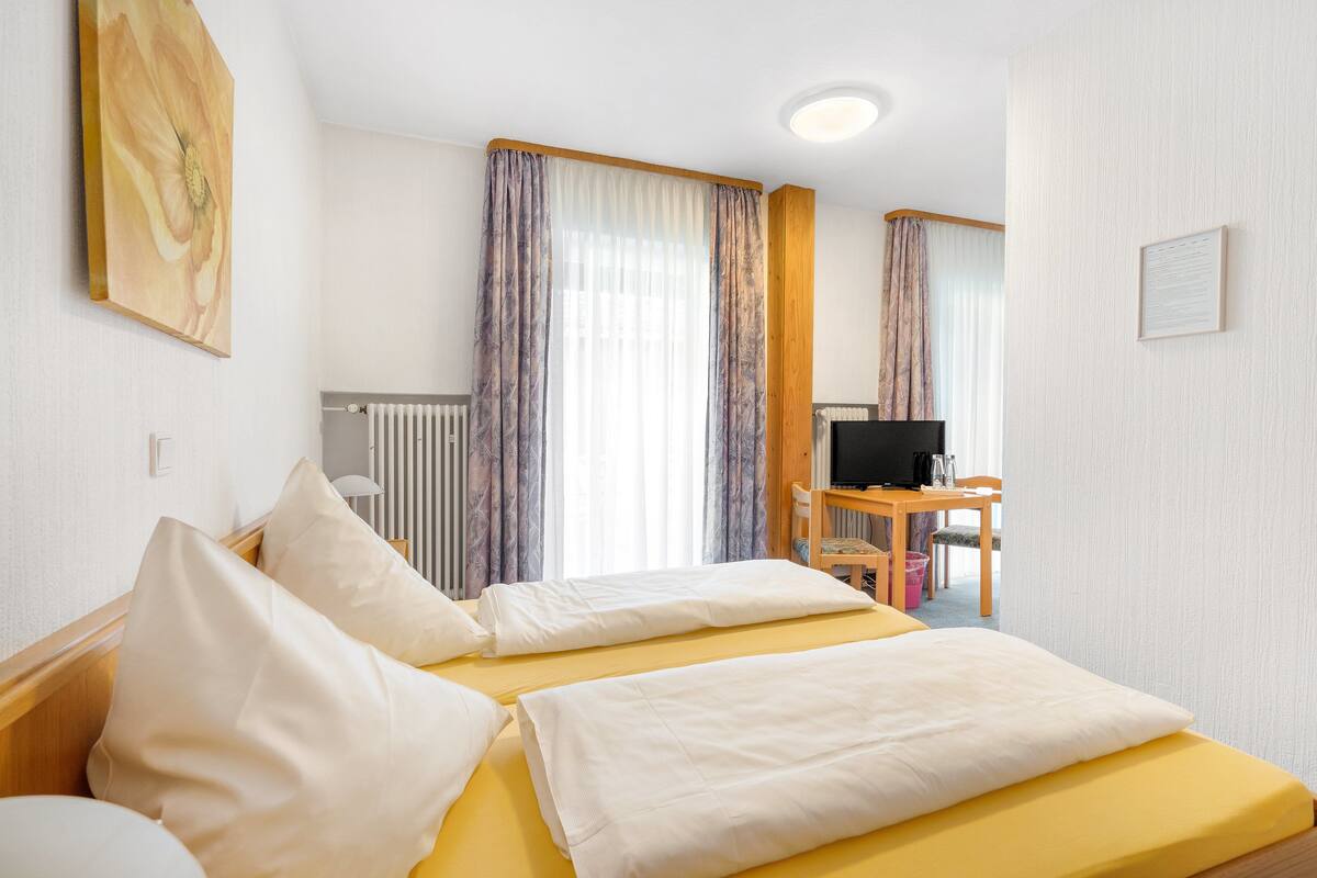 A hotel room with two beds, a desk, a chair, a television, and a radiator.