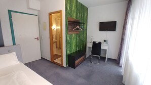 Une chambre d’hôtel comprenant un lit, un bureau avec une chaise, une télévision et une salle de bain avec un miroir et un lavabo.