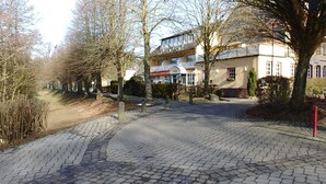 Un chemin pavé bordé d’arbres et un bâtiment doté d’un toit en pente et de grandes fenêtres.