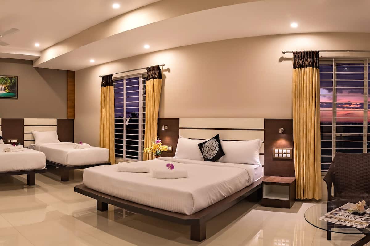 A hotel room with two single beds, a double bed, a glass coffee table, a chair, and a view of the sunset through the window.