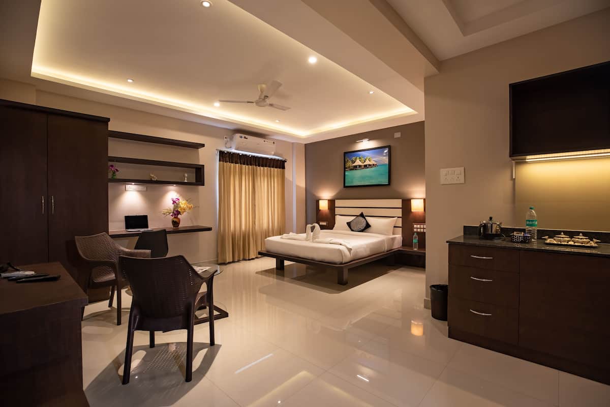 A modern hotel room with a bed, desk, chairs, and a TV.