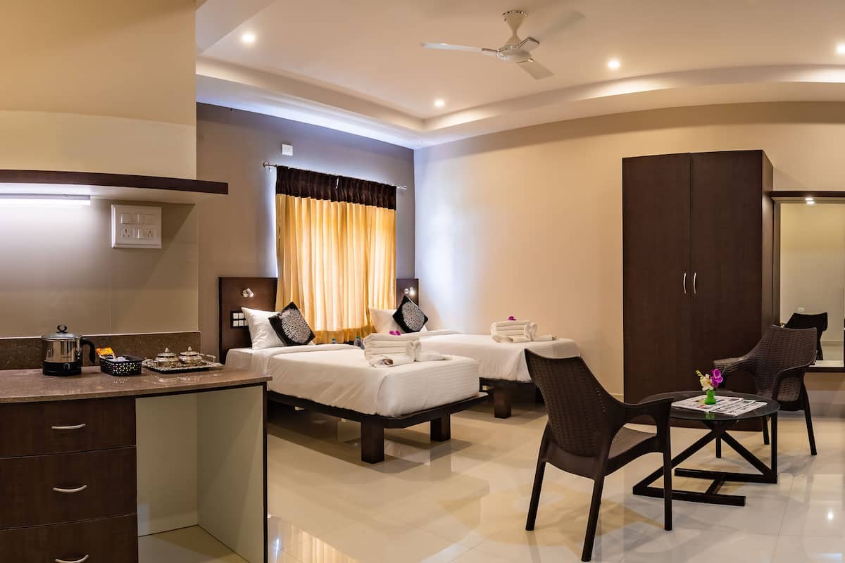 A hotel room with a kitchenette, two beds, a dining area, and a large wardrobe.