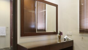 A bathroom with a wooden vanity, a mirror, a vase with flowers, a hairdryer, and a towel hanging on the wall. - Gurney 4 Plus 1 Bali Style Tranquil Villa (George Town)