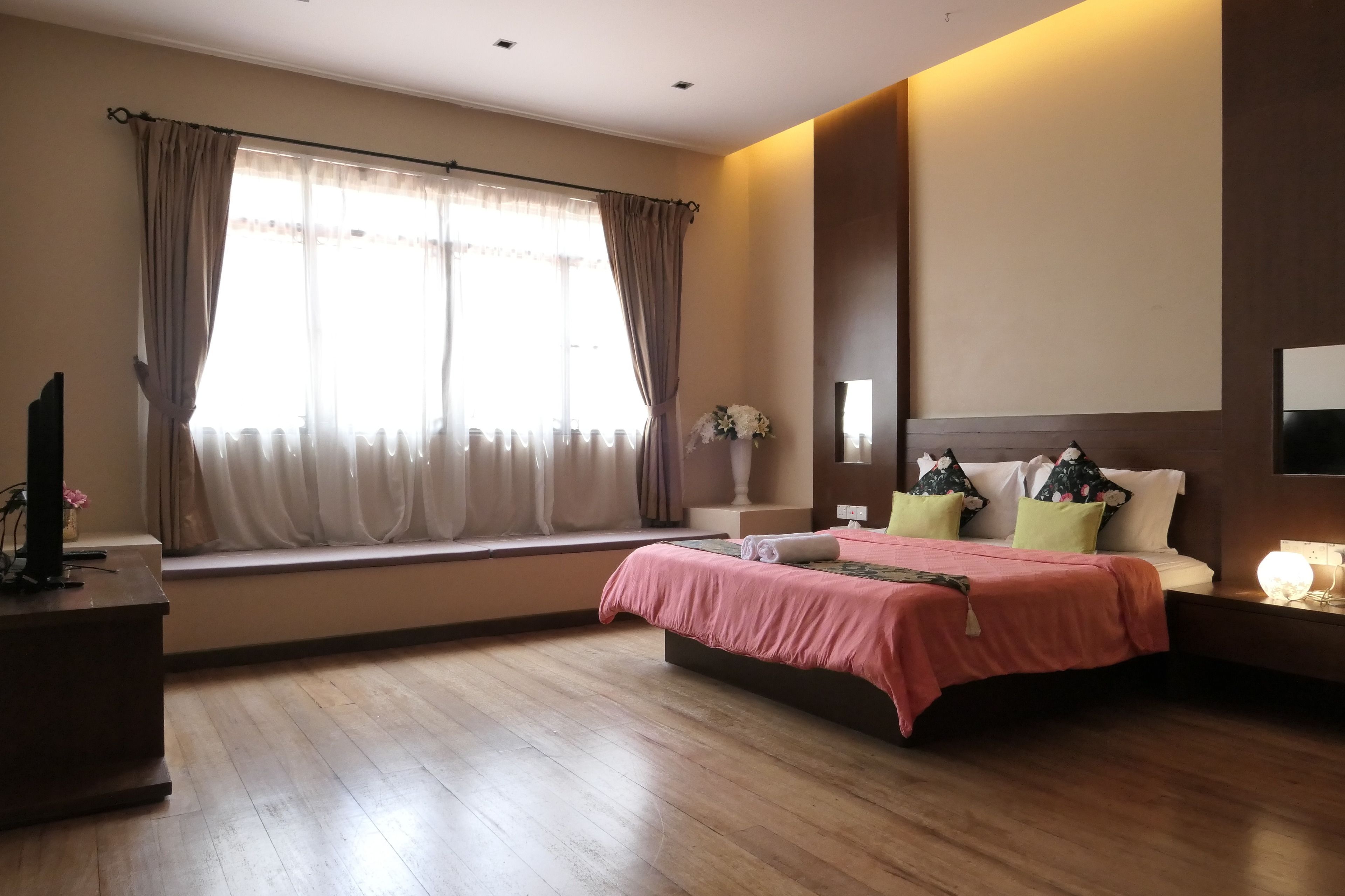 A bedroom with a bed, a nightstand, a lamp, a window with curtains, and a TV on a stand.