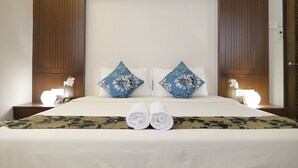 A neatly made bed with floral pillows, a bedside table with a lamp, and a nightstand with a vase of flowers. - Gurney 4 Plus 1 Bali Style Tranquil Villa (George Town)