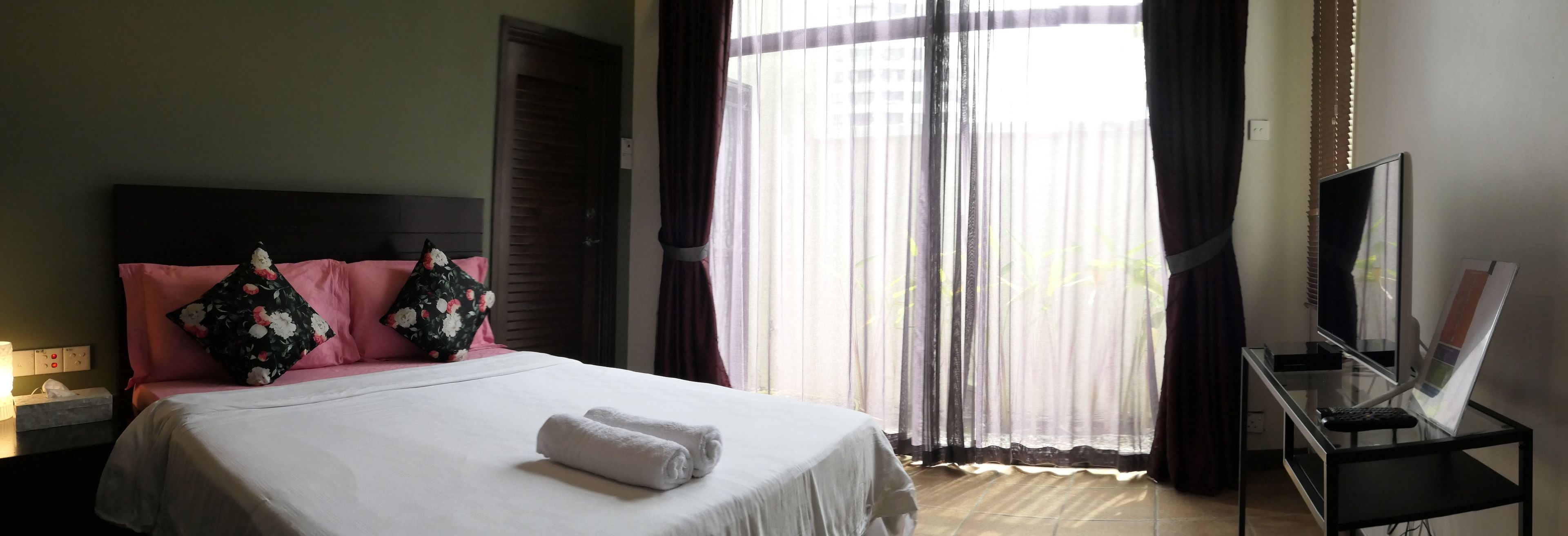A hotel room with a bed, pillows, a TV on a stand, and a window with curtains.