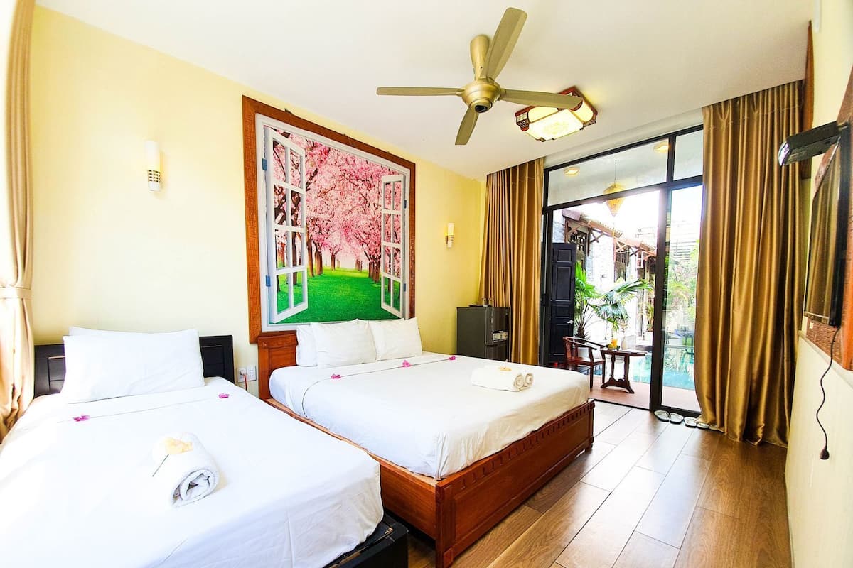 A hotel room with two beds, a ceiling fan, a painting of a cherry blossom tree, and a view of a pool through a glass door.