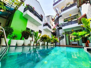 A modern indoor pool area with a clear pool, surrounded by potted plants and a spiral staircase. - Anh Family Homestay (Da Nang)