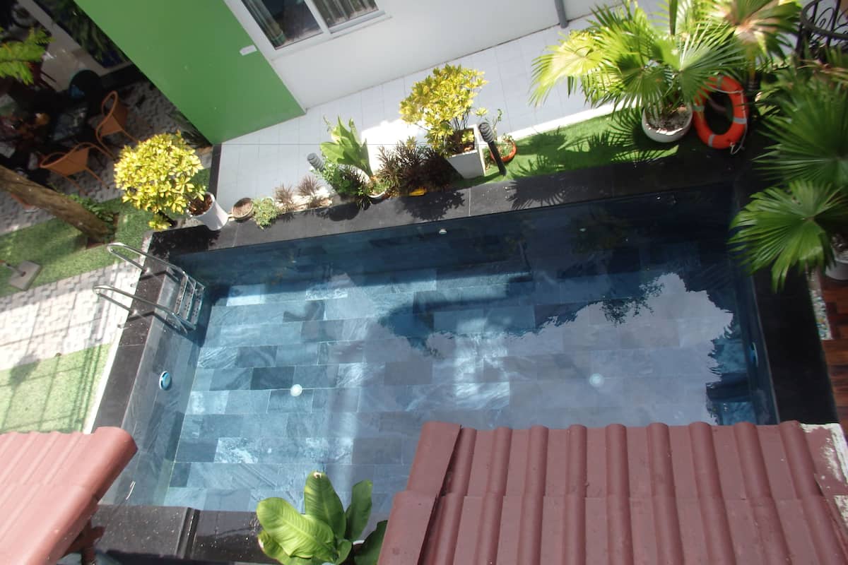 A swimming pool with a tiled deck, surrounded by potted plants and a red safety ring.
