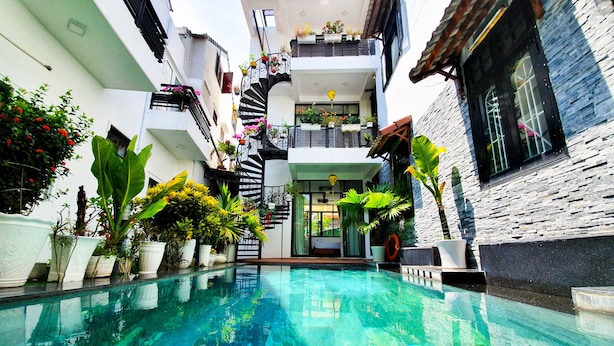 A swimming pool with a clear blue water, surrounded by potted plants and a staircase leading to a balcony with hanging plants. - Anh Family Homestay (Da Nang)