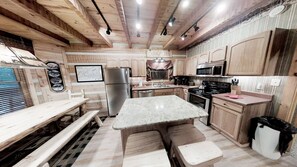 A cabin-style kitchen with wooden cabinets, a granite countertop, stainless steel appliances, and a dining area with a bench. - Streamsong Secluded Creek View Cabin with Hot Tub and Pool Table by RedAwning (Sevierville)