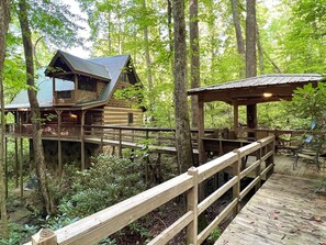 A wooden cabin with a deck and a covered seating area surrounded by forest. - Streamsong Secluded Creek View Cabin with Hot Tub and Pool Table by RedAwning (Sevierville)