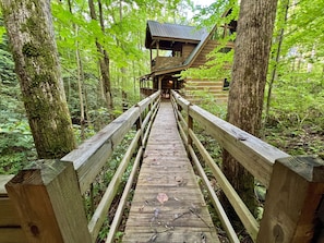 A wooden bridge leading to a treehouse with a metal roof, surrounded by a forest. - Streamsong Secluded Creek View Cabin with Hot Tub and Pool Table by RedAwning (Sevierville)