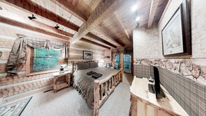 Ein rustikaler Holzraum mit einem Bett, einem Fenster mit Vorhängen, einem kleinen Tisch mit einer Lampe und einem an der Wand hängenden Bild.