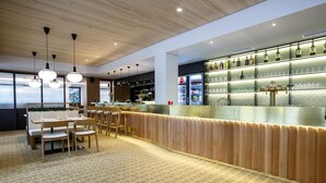 A modern bar area with a wooden counter, bar stools, and a patterned floor. - Hotel Rajka (Valasske Mezirici)