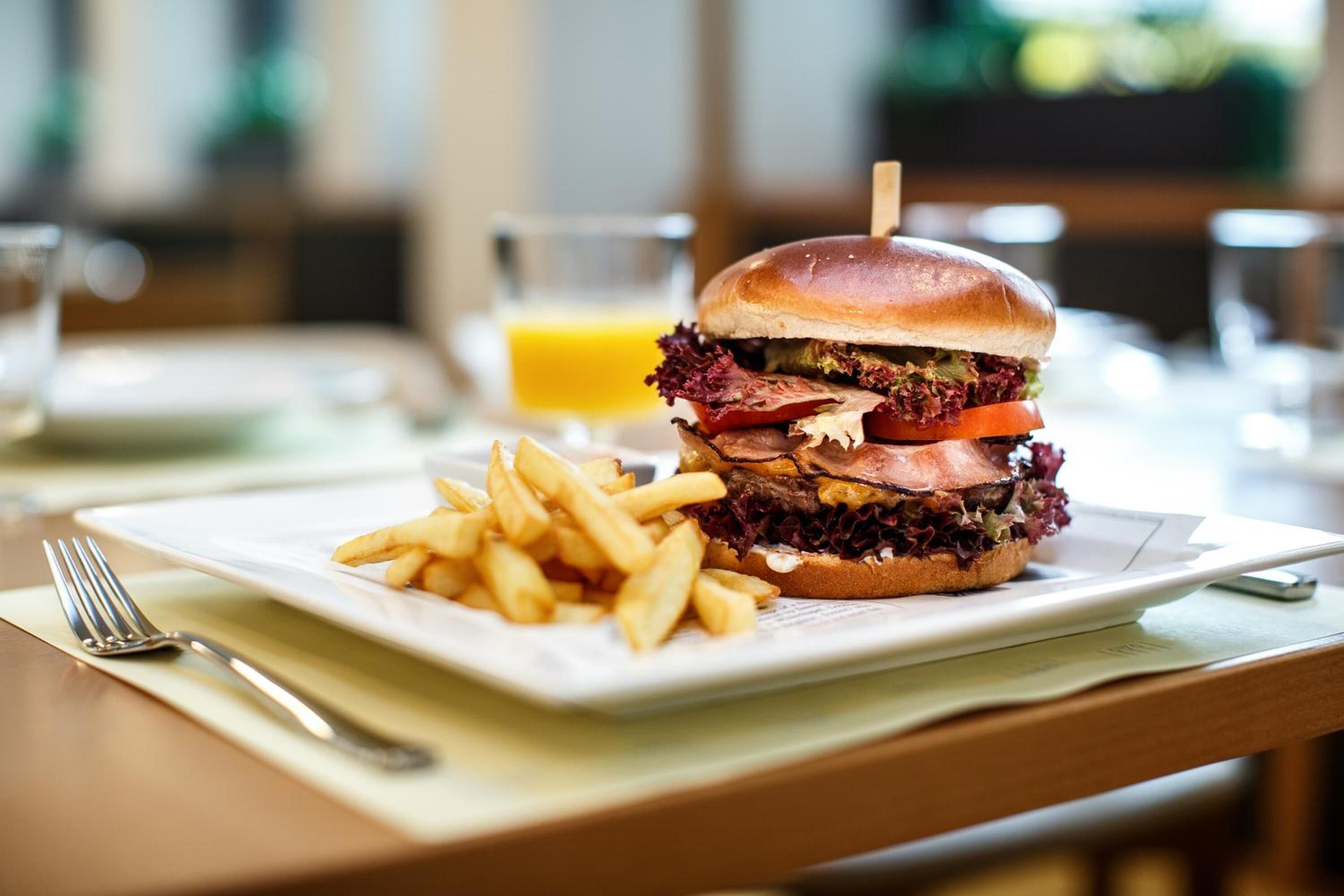 A meal consisting of a sandwich and fries on a white plate, with a fork and knife on a napkin beside it.