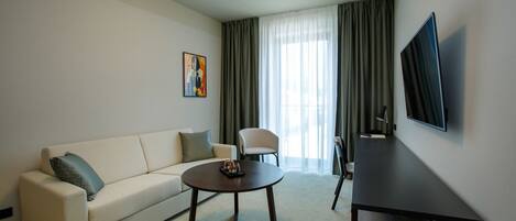 A modern living room with a sofa, armchair, coffee table, TV, and a painting on the wall.