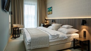 A modern hotel room with a large bed, a desk with a chair, a flat-screen TV, and a painting on the wall. - Hotel Rajka (Valasske Mezirici)