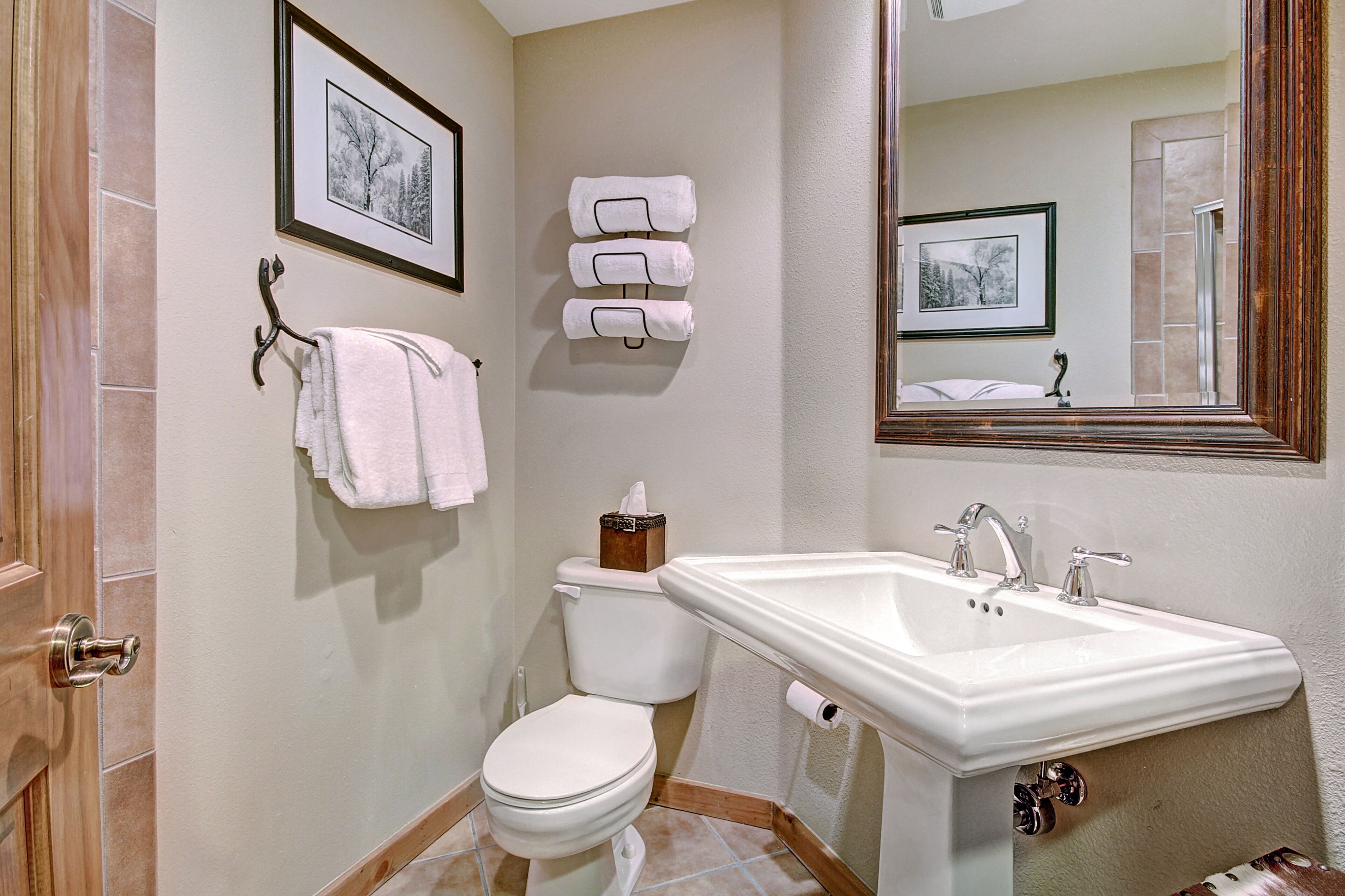 A bathroom with a white sink, toilet, and a framed picture above the toilet.