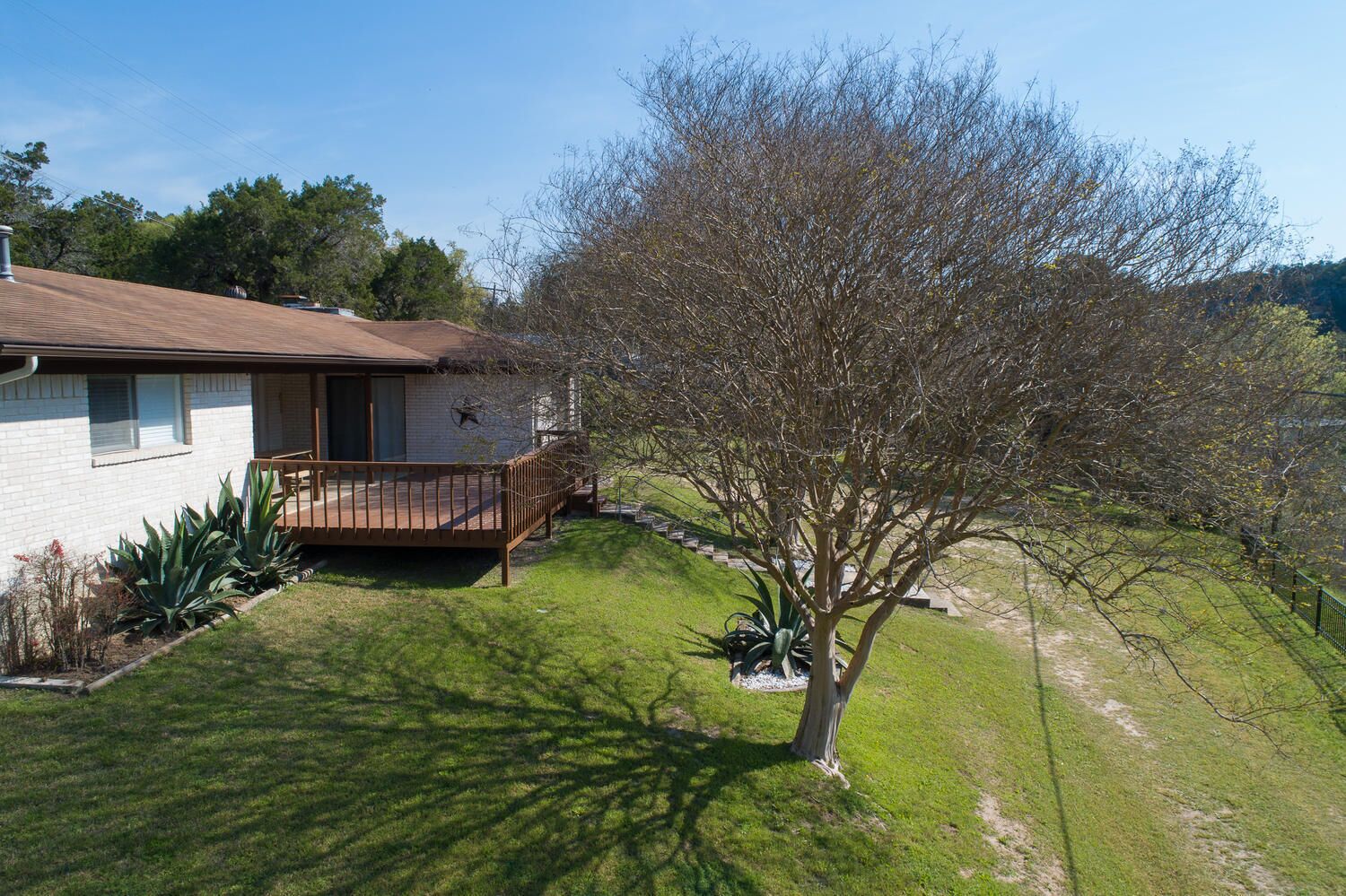 A single-story house with a fenced backyard, a wooden deck, and a small tree.