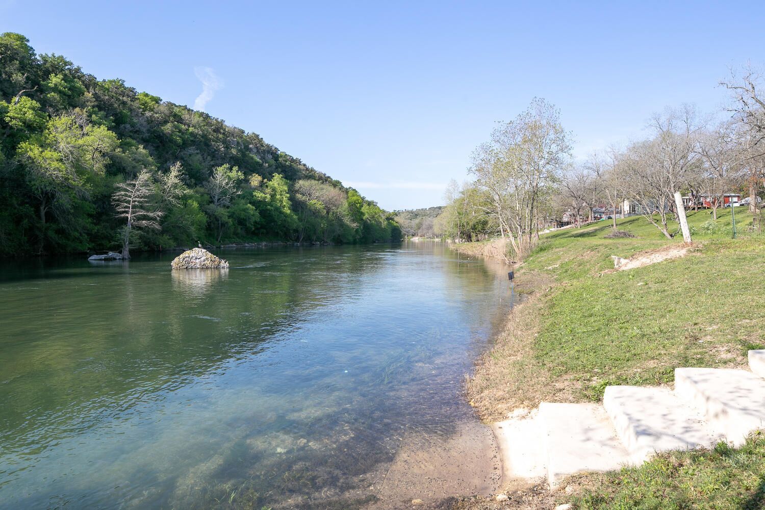 A river with clear water, a small island, and a grassy bank with steps leading down to the water.